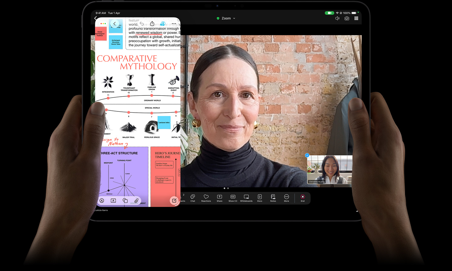 iPad Pro, front exterior, space black color, left and right hands holding in landscape orientation, rounded corners, black display bezel, display showing a FaceTime conversation being live translated, and an educational app showing a presentation of 'Comparative Mythology' with text, diagrams, and handwritten notes