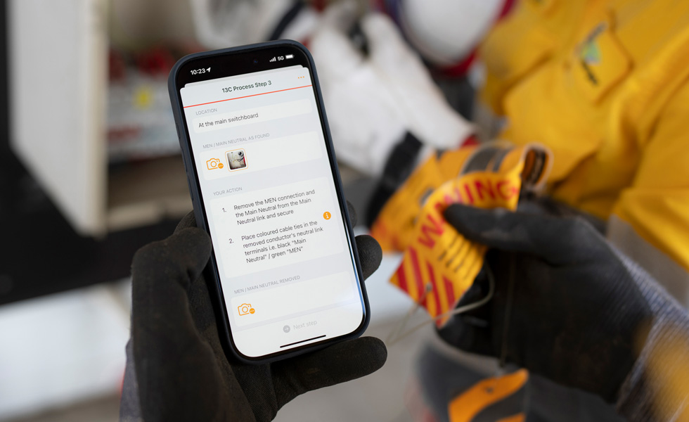 Kädet pitelevät iPhonea, joka näyttää ohjeet kytkintaulutestin suorittamiseen, ja ruudulla on teksti ”13C Process Step 3”