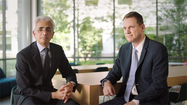 Two people in suits sitting at a table.