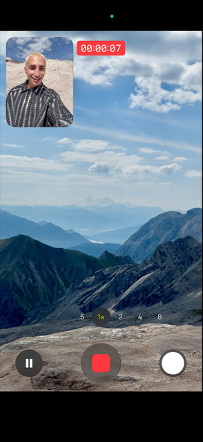 A person demonstrates Dual Capture video by recording himself with the front camera and simultaneously recording the scenic mountains with rear camera