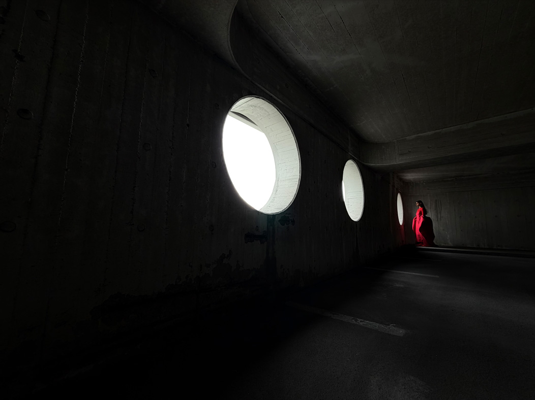 A woman wearing a long red dress stands in an empty room being photographed. The Photos app toggles through the focal lengths to demonstrate the capabilities of the pro camera system, showcasing: 13mm