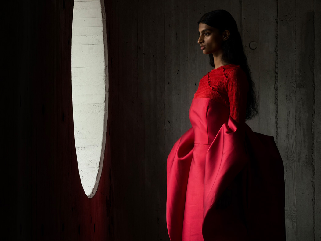 A woman wearing a long red dress stands in an empty room being photographed. The Photos app toggles through the focal lengths to demonstrate the capabilities of the pro camera system, showcasing: 200mm