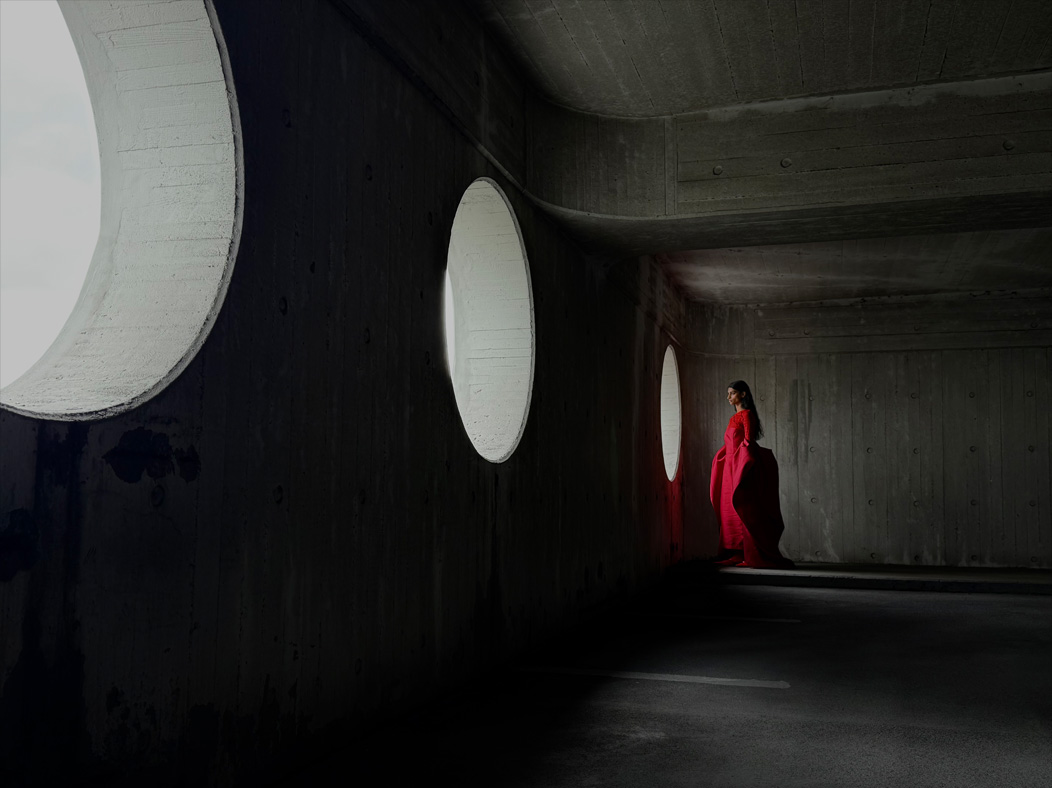 A woman wearing a long red dress stands in an empty room being photographed. The Photos app toggles through the focal lengths to demonstrate the capabilities of the pro camera system, showcasing: 35mm