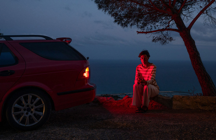 A photo of a car stranded by the side of a road, one person by the car using Roadside Assistance via satellite on iPhone