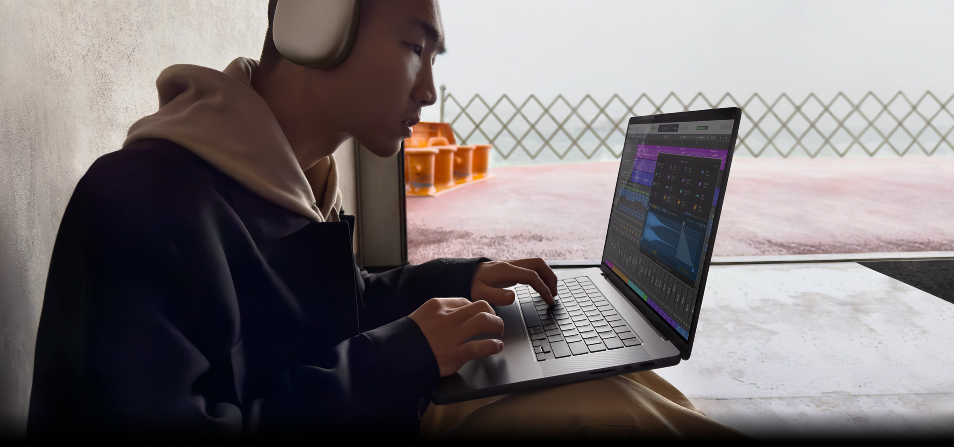 Side profile of a person wearing AirPods Max using Logic Pro on a MacBook Pro 16, screen shows Logic Pro workspace