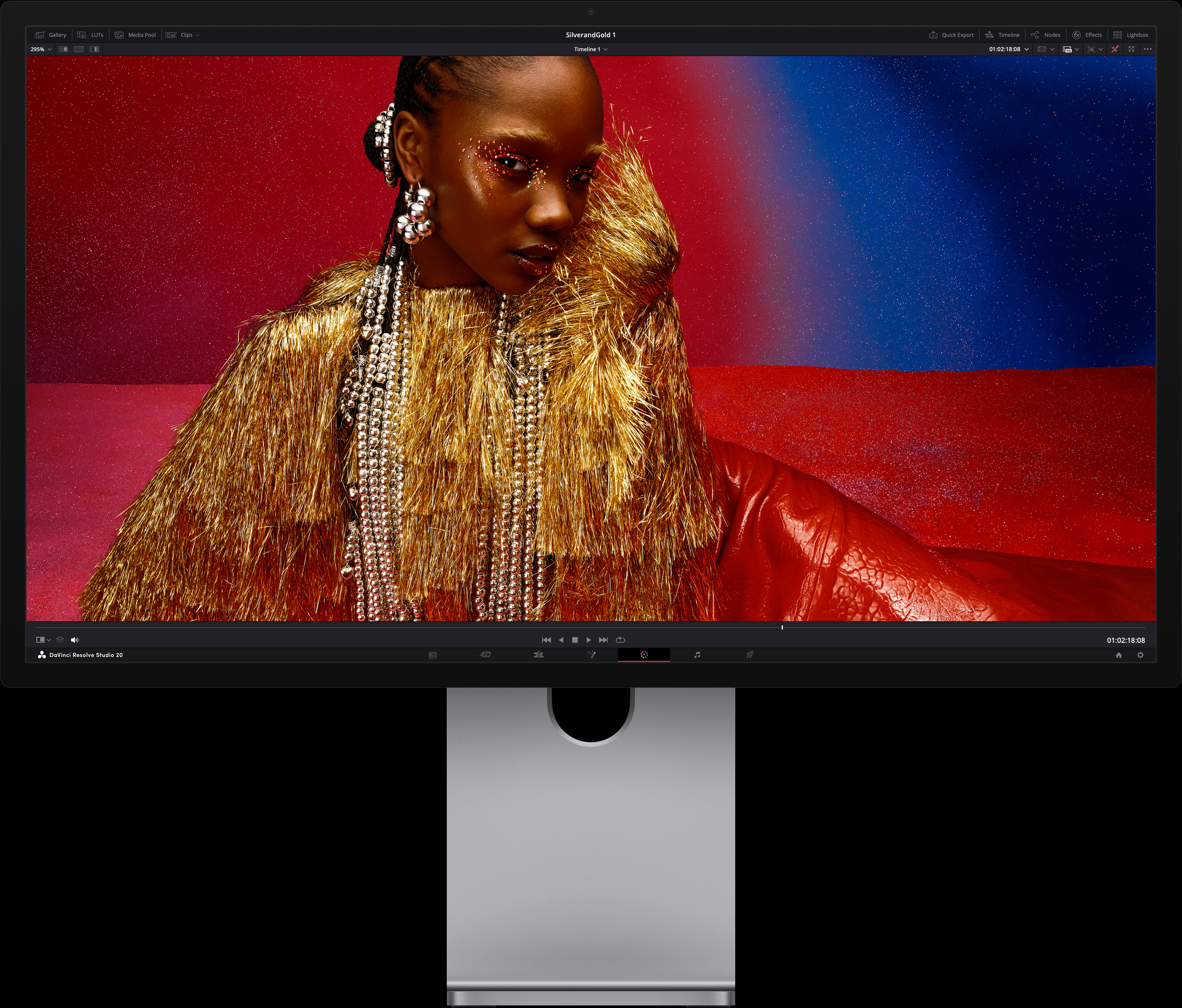 Osoba v jasných červených šatách s výraznými kovovými doplnkami sedí pred modročerveným pozadím, čo znázorňuje kvalitu obrazu displeja Studio Display XDR